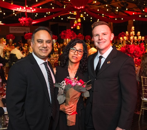 Two men on each side of a woman holding a bouquet of red flowers.